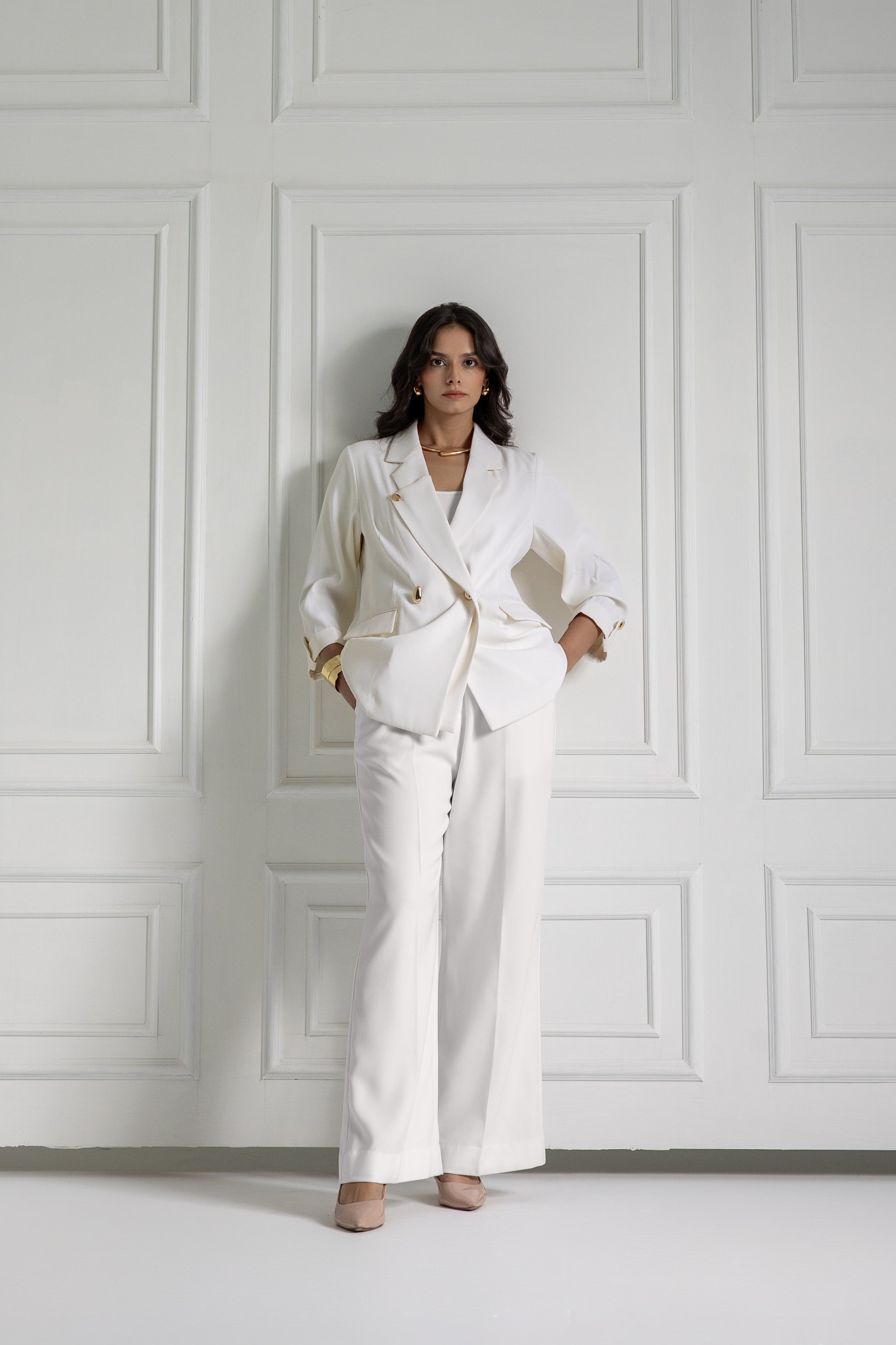 Woman in a white suit standing against a white paneled wall