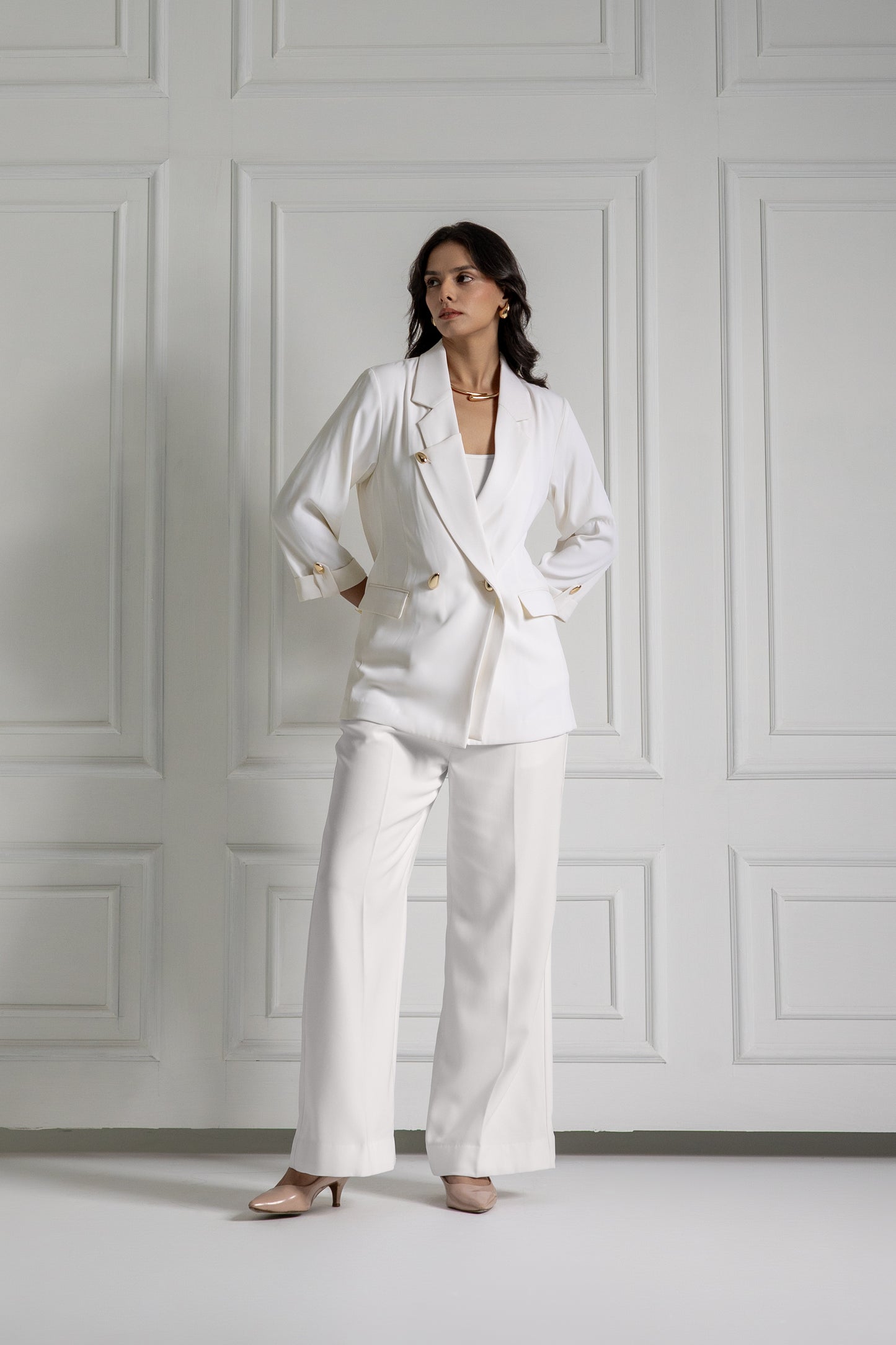 Woman wearing a white suit standing against a white paneled wall.
