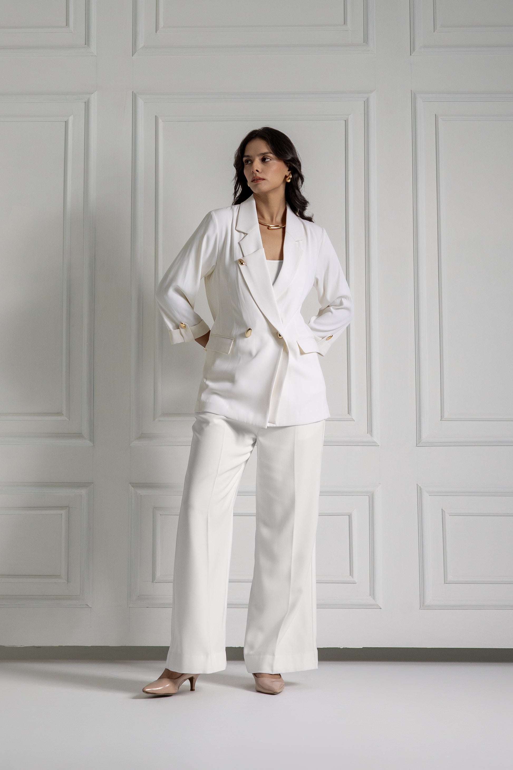 Woman wearing a white suit standing against a white paneled wall.