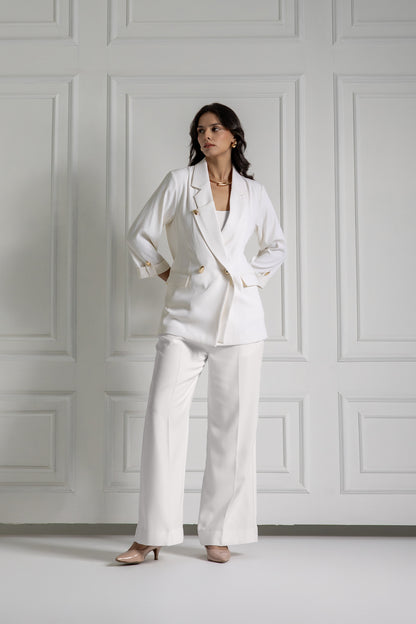 Woman wearing a white suit standing against a white paneled wall.