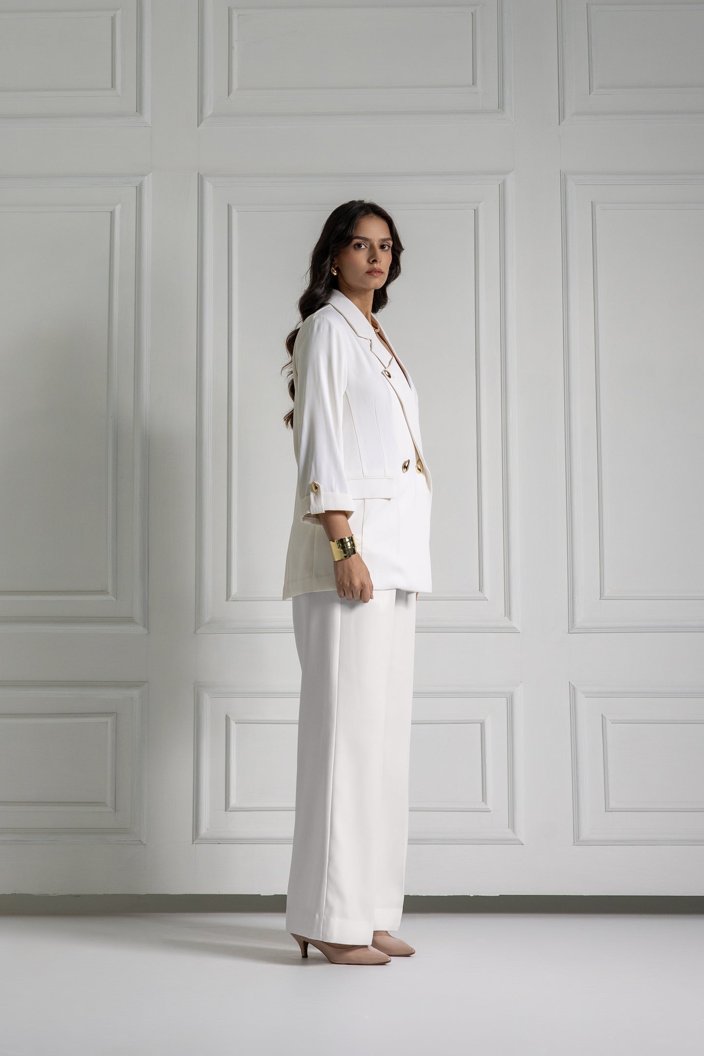 Woman in a white suit standing against a gray paneled wall