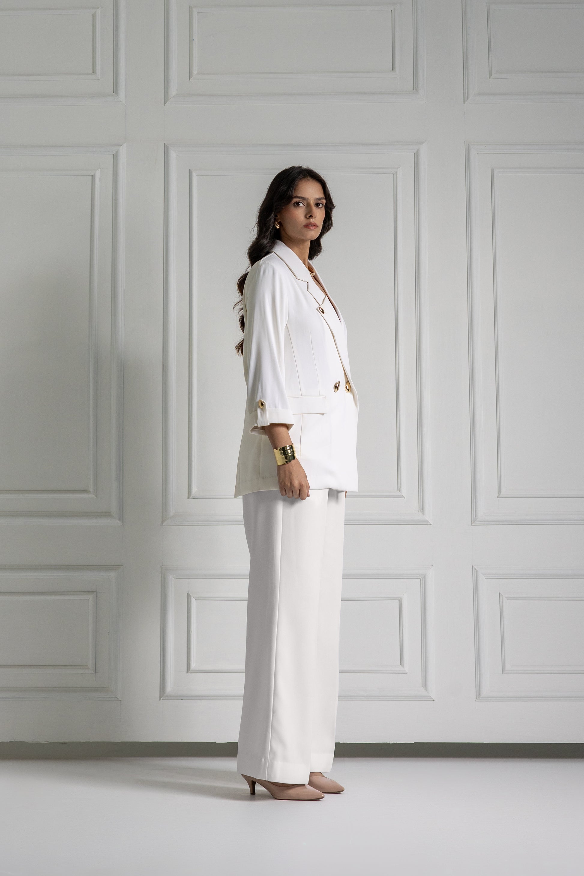 Woman in a white suit standing against a gray paneled wall