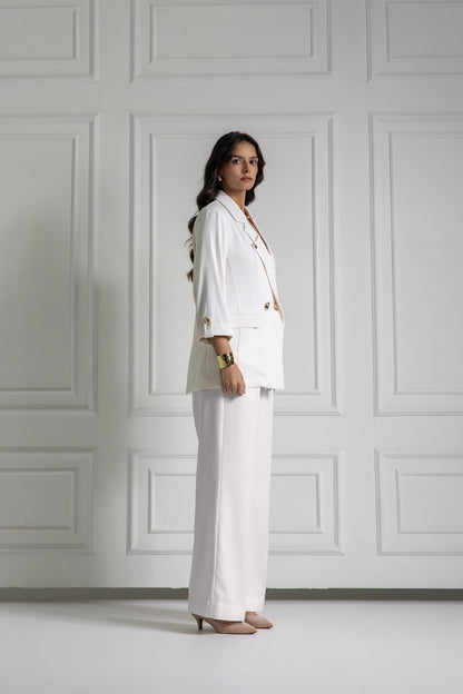 Woman in a white suit standing against a gray paneled wall