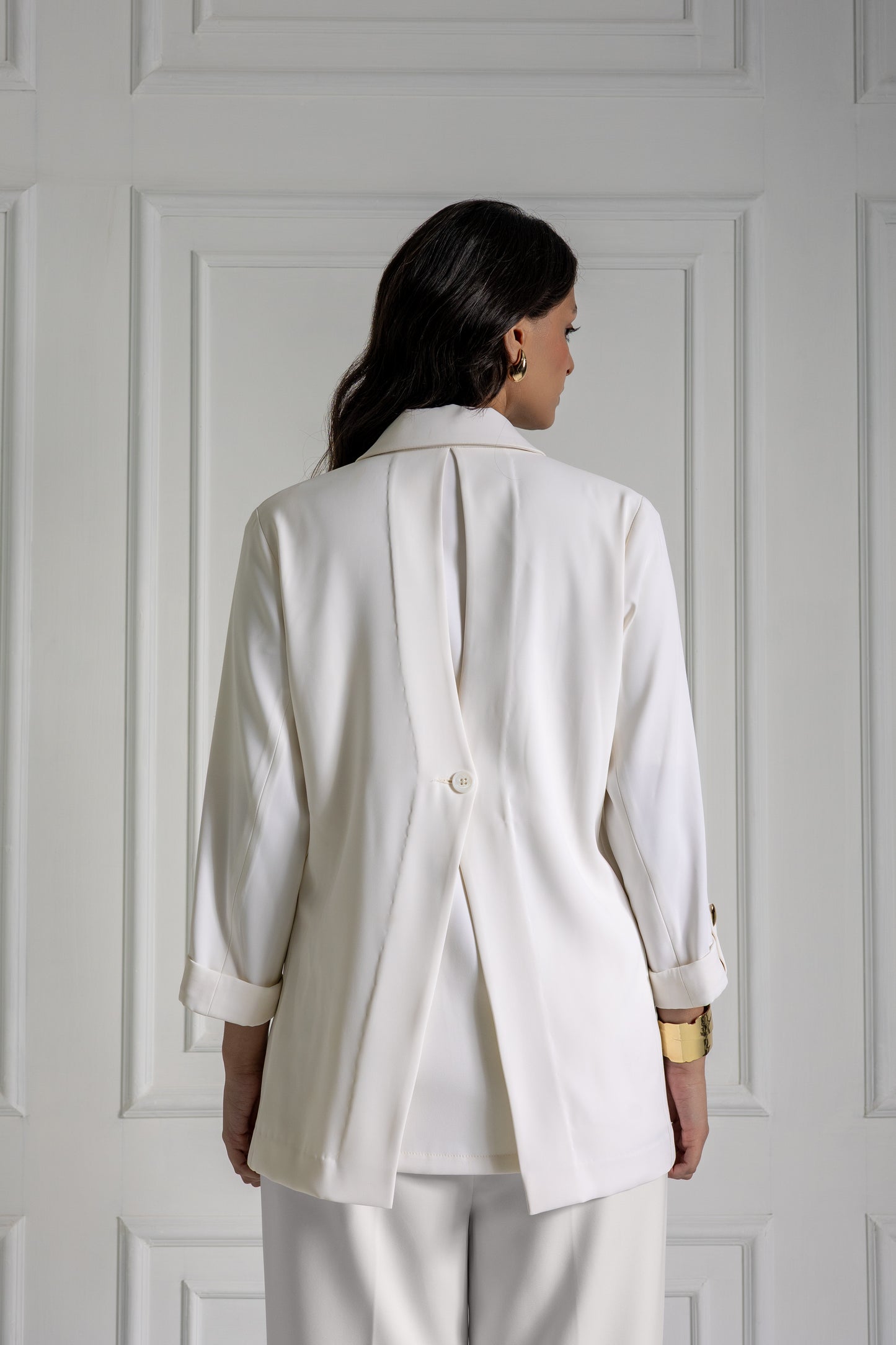 Person wearing a white blazer and pants against a white paneled wall